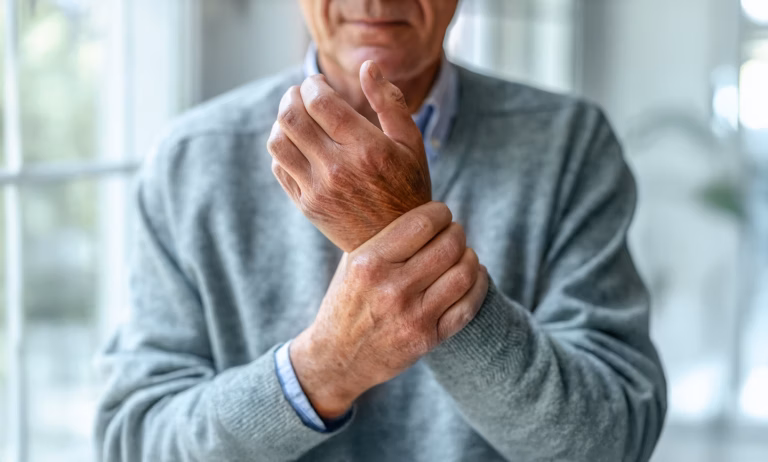 Medianuslähmung - Ein älterer Mann im grauen Pullover hält mit der linken Hand sein rechtes Handgelenk.