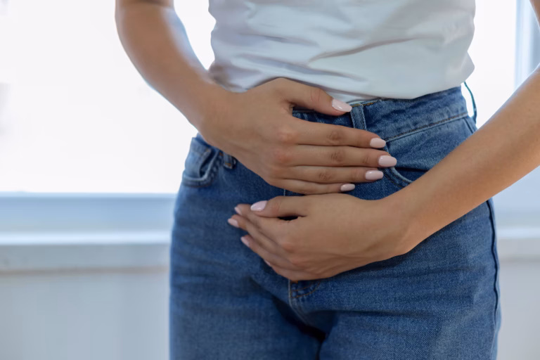 Harnverhalt: Korpusbild einer Frau in Jeans und hellem T-Shirt, die beide Hände schützend vor den Bauch hält.