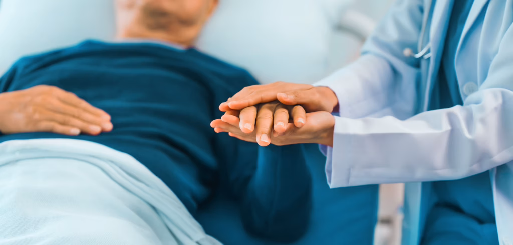 Lähmung nach Tumor-OP: Arzt hält Hand von einem im Krankenhaus liegendem Patienten.